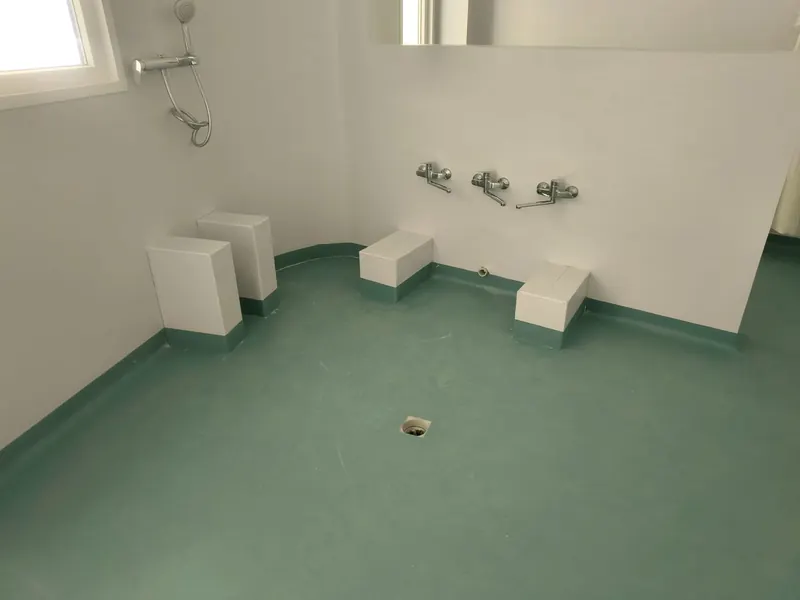 Bagno d'asilo in linoleum verde acqua, il pavimento sale sulle pareti e sui gradini