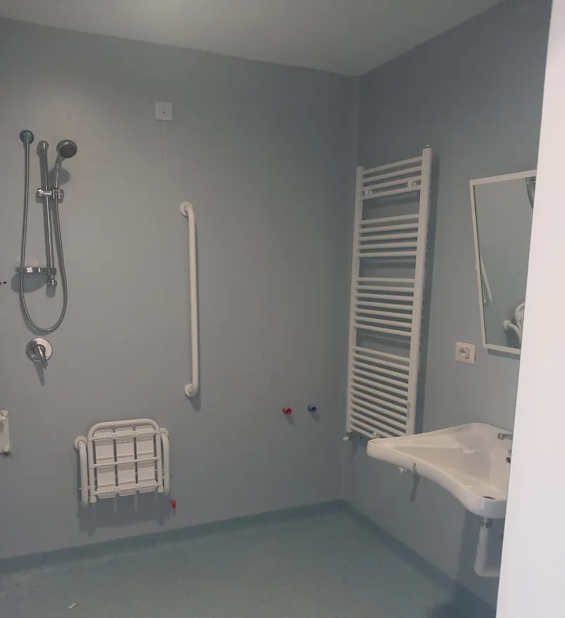 Bagno accessibile con doccia e seggiolino, pavimento in PVC granigliato