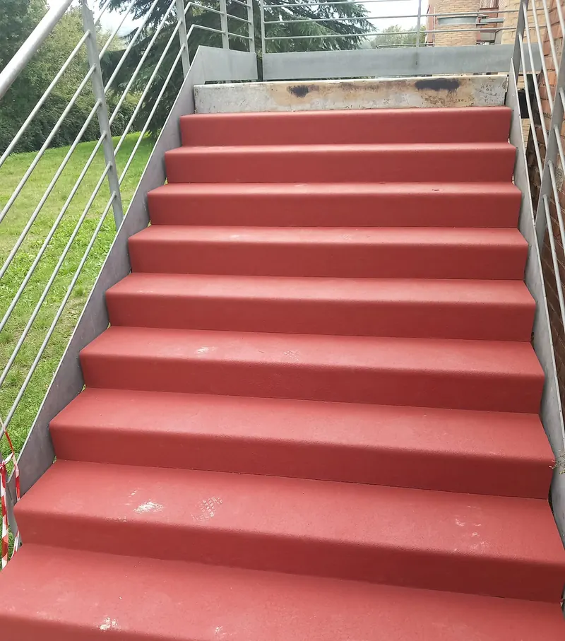 Scala esterna in gomma rossa con ringhiera, accanto a un prato