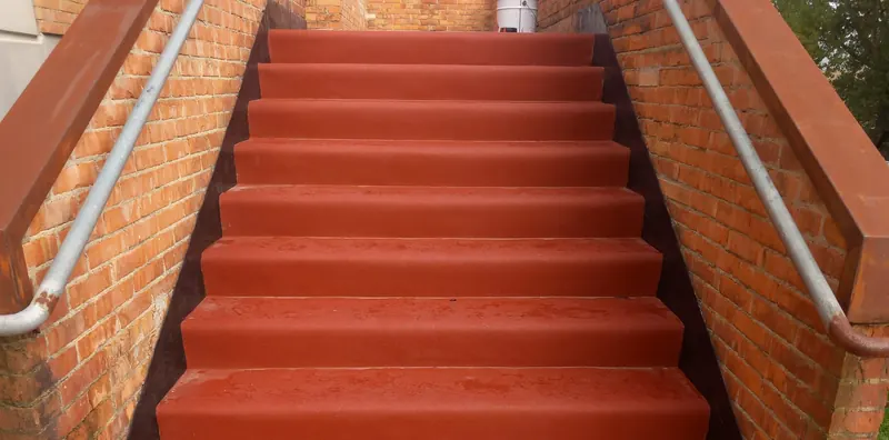 Scala esterna rivestita in gomma rossa tra due muri di mattoni
